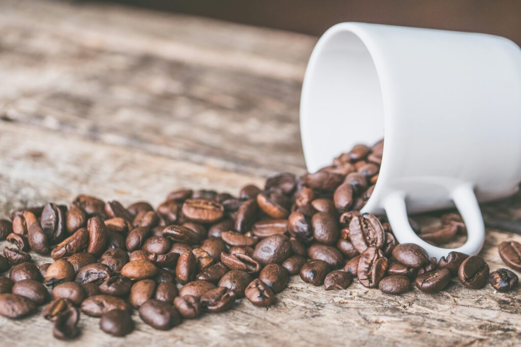 Coffee beans spilling from a white mug on a rustic wooden surface, embodying a cozy and warm atmosphere.